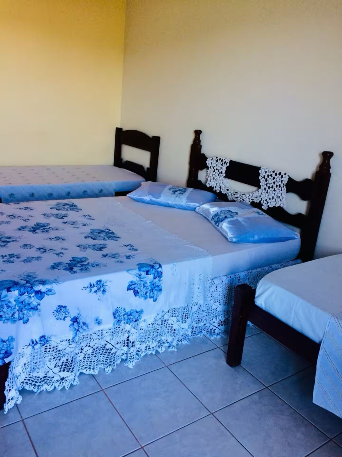Quarto com cama de casal, cabeceira de madeira e colcha rendada azul